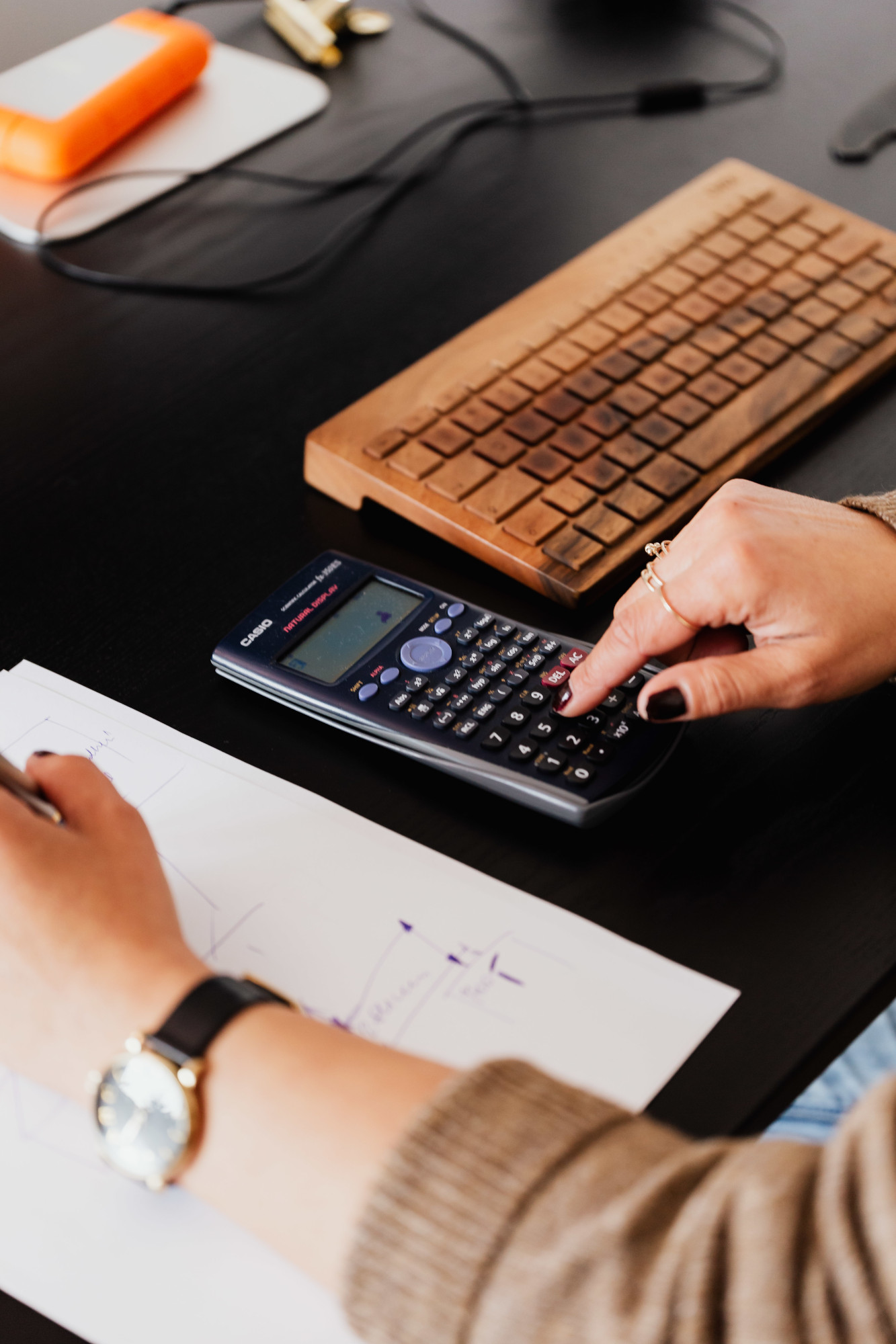 Person using calculator on desk with keyboard